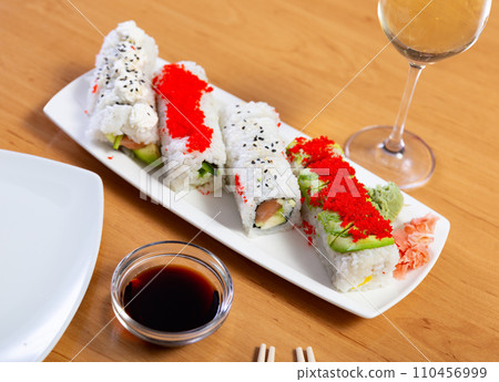 Sushi roll with red tobiko caviar on white plate on bamboo wooden table. Sushi roll with red tobiko caviar on white plate on bamboo wooden table. 110456999