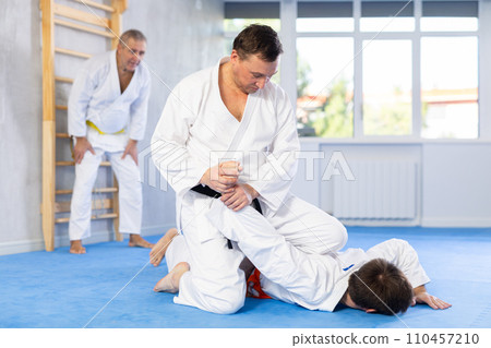 Focused adult jiu-jitsu fighter performing painful armlock during sparring 110457210