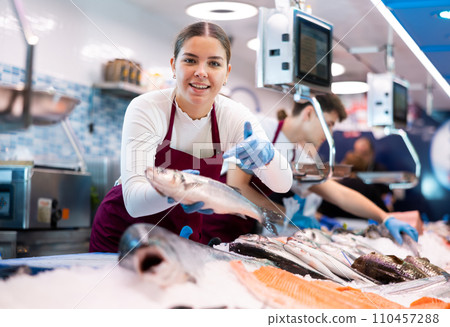 Positive saleswoman demonstrating seabass in fish store Positive saleswoman demonstrating seabass in fish store 110457288