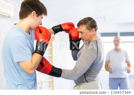Young boxer in sportswear doing boxing sparring with trainer in the gym Young boxer in sportswear doing boxing sparring with trainer in the gym 110457364