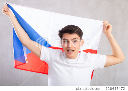 Happy young man holding flag of Czechia against unicoloured background Happy young man holding flag of Czechia against unicoloured background 110457472