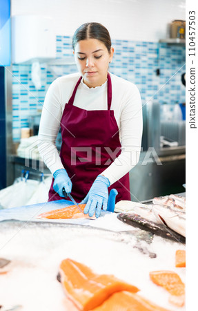 Female seller with knife cut fish in supermarket near counter Female seller with knife cut fish in supermarket near counter 110457503