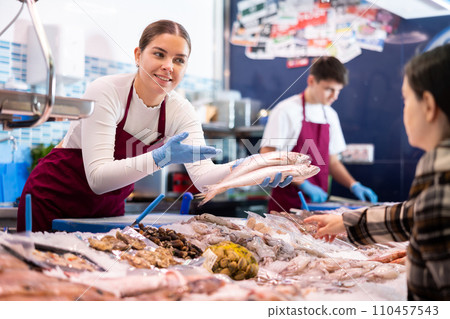 Smiling saleswoman demonstrating red snapper to purchaser in fish store 110457543