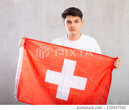 Portrait of calm, balanced young man in casual clothes with fabric of national Swiss flag. 110457592