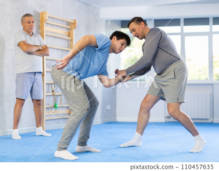 Two athlete men of different age in sportswear practicing self-defense sparring in hall Two athlete men of different age in sportswear practicing self-defense sparring in hall 110457635