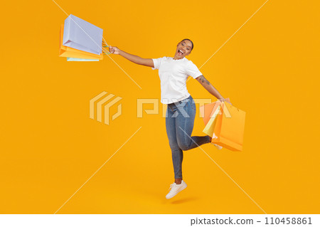 Happy black buyer woman jumps holding paper shopping bags, studio Happy black buyer woman jumps holding paper shopping bags, studio 110458861