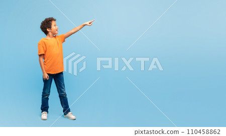 Excited boy pointing in the air at free space on blue backdrop 110458862