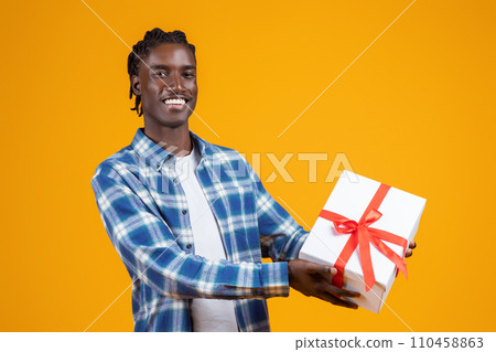 Happy young black man extending white gift box with red ribbon 110458863