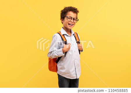 Happy black schoolboy with backpack smiling on yellow backdrop 110458885