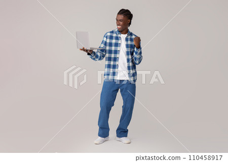 Portrait Of Joyful Black Man Celebrating Success With Laptop, Raising Clenched Fist Portrait Of Joyful Black Man Celebrating Success With Laptop, Raising Clenched Fist 110458917
