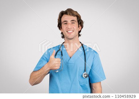 Smiling european man nurse giving thumbs up on grey background 110458929
