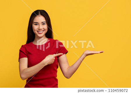 Cheerful asian woman pointing at copy space on her palm Cheerful asian woman pointing at copy space on her palm 110459072