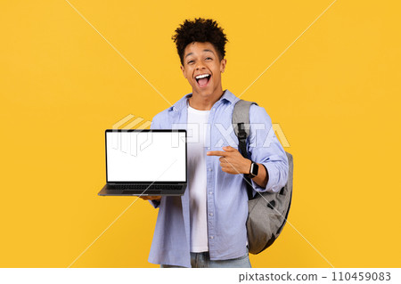 Ecstatic male student pointing at laptop screen on yellow, mockup 110459083