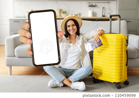 Cheerful young tourist woman wearing straw hat showing blank smartphone at camera 110459099