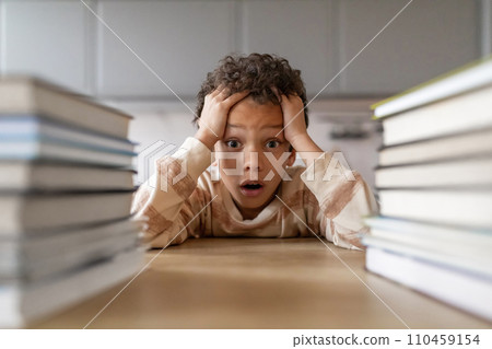 Stressed black boy surrounded by towering stacks of books Stressed black boy surrounded by towering stacks of books 110459154
