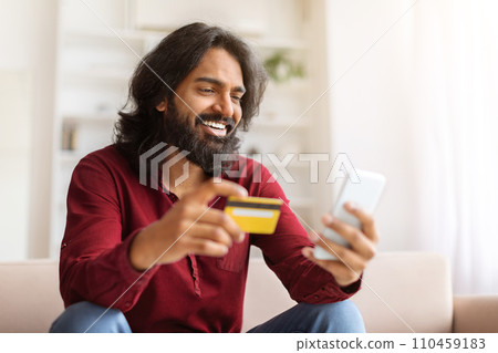 Positive indian guy enjoying newest shopping application Positive indian guy enjoying newest shopping application 110459183