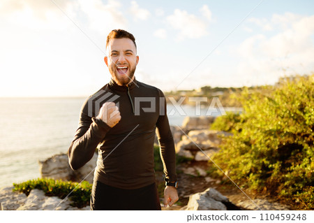 Ecstatic man celebrating with fist pump by the ocean Ecstatic man celebrating with fist pump by the ocean 110459248