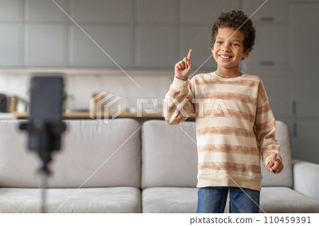 Cheerful little black boy with curly hair recording video blog at home 110459391