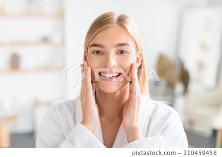 Portrait of blonde lady touches cheeks enjoys morning skincare indoor 110459458