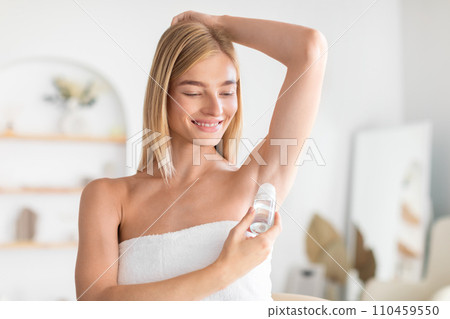 Pretty blonde woman applying roll-on antiperspirant under her arms indoors Pretty blonde woman applying roll-on antiperspirant under her arms indoors 110459550