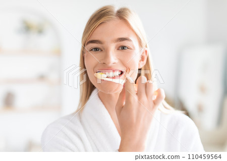 Portrait of pretty blonde woman attentively cleaning her teeth indoors 110459564