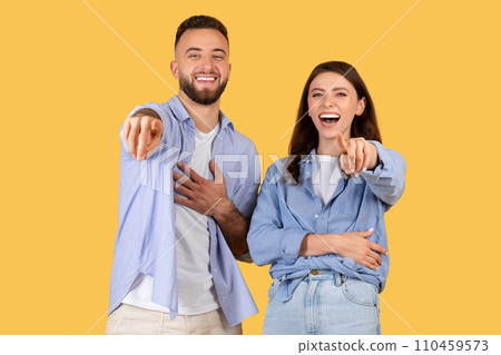 Laughing couple pointing at camera in casual clothes on yellow background 110459573