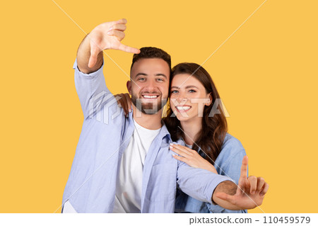 Happy couple making frame with hands, yellow backdrop Happy couple making frame with hands, yellow backdrop 110459579