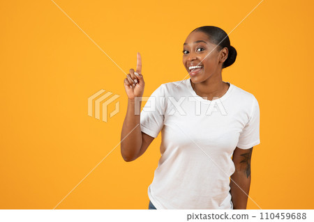 Happy black lady pointing finger upwards on yellow studio background Happy black lady pointing finger upwards on yellow studio background 110459688
