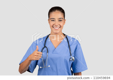 Confident European millennial doctor in blue scrubs giving a thumbs-up Confident European millennial doctor in blue scrubs giving a thumbs-up 110459694