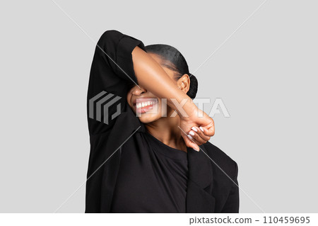 Joyful African American businesswoman playfully covering her eyes with one arm 110459695