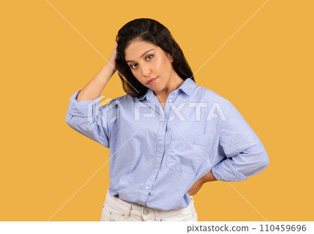 A confident young woman with dark hair wearing a casual blue shirt poses thoughtfully 110459696