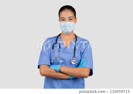 Glad caucasian millennial lady doctor or nurse in blue uniform, protective mask, gloves with crossed arms Glad caucasian millennial lady doctor or nurse in blue uniform, protective mask, gloves with crossed arms 110459715