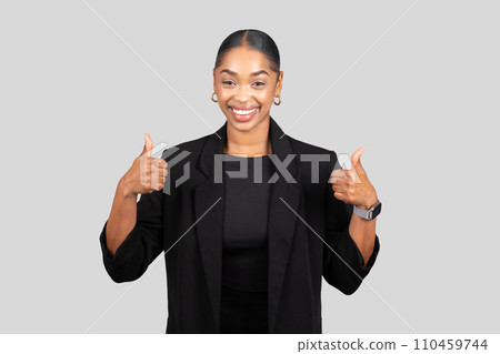 Enthusiastic African American woman in formal attire giving two thumbs up with a radiant smile 110459744