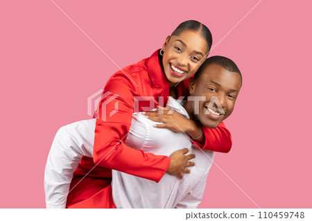 Joyful black couple with woman piggybacking on man against pink backdrop Joyful black couple with woman piggybacking on man against pink backdrop 110459748