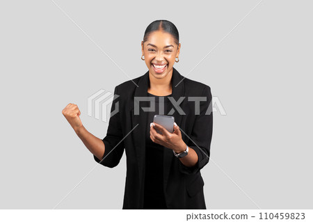 Joyful African American businesswoman in a black blazer showing a triumphant gesture Joyful African American businesswoman in a black blazer showing a triumphant gesture 110459823