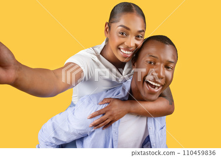 Black couple taking selfie, joyful expressions on yellow background 110459836