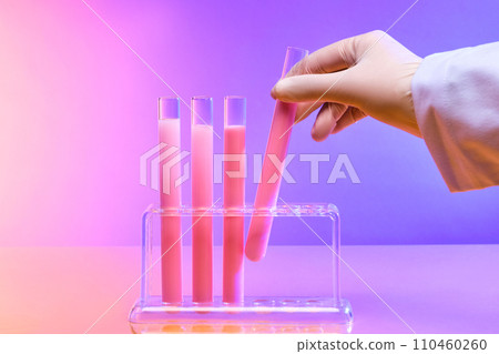 A hand is holding a test tube containing pink liquid. Purple pink gradient background. Laboratory space viewed from the front. Copy for advertising. 110460260