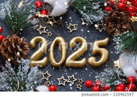 The golden figures 2025 made of candles on a black stone slate background are decorated with a festive decor of stars, sequins, fir branches, balls and garlands. Greeting card, happy New Year. The golden figures 2025 made of candles on a black stone slate background are decorated with a festive decor of stars, sequins, fir branches, balls and garlands. Greeting card, happy New Year. 110462547