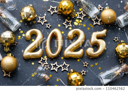 The golden figures 2025 made of candles on a black stone slate background are decorated with a festive decor of stars, sequins, fir branches, balls and garlands. Greeting card, happy New Year. The golden figures 2025 made of candles on a black stone slate background are decorated with a festive decor of stars, sequins, fir branches, balls and garlands. Greeting card, happy New Year. 110462562