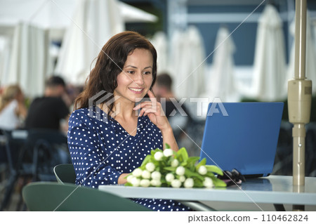 Young happy woman working remotely on laptop computer sitting at outdoor restaurant table. Doing business online concept Young happy woman working remotely on laptop computer sitting at outdoor restaurant table. Doing business online concept 110462824