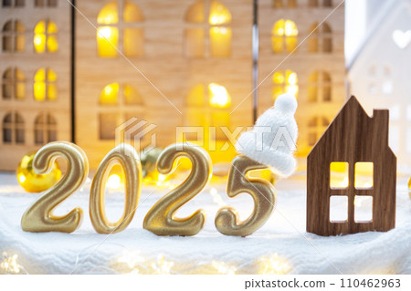 Golden figures number 2025 and tiny home on background of cozy windows of a house with warm light with festive decor of stars,snow and garlands. Greeting card, Happy New Year, cozy home 110462963