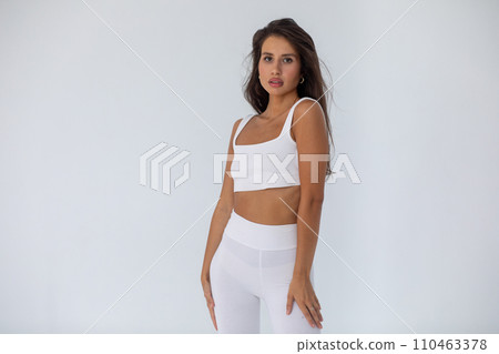 Beautiful brunette girl in a white top and tights posing on white background 110463378