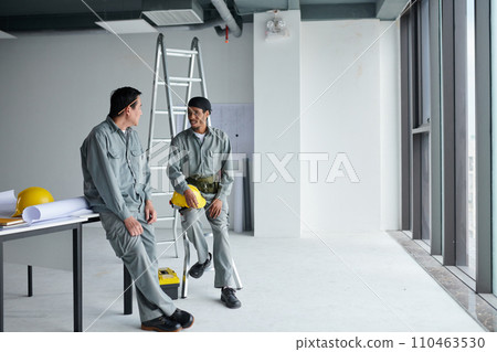 Builders in grey uniform talking after finishing work in building after construction 110463530