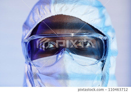 Extreme close up shot of Black man laboratory technician in hazmat suit and protective glasses looking at camera 110463712