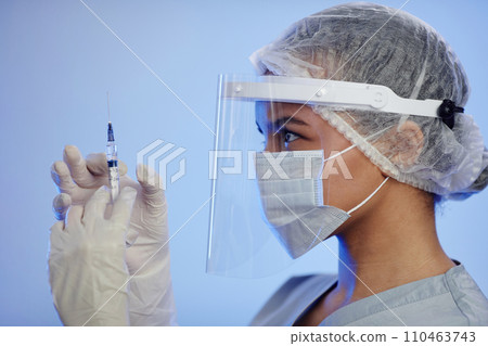 Side view of female nurse wearing protective medical face shield and mask while removing air bubbles from syringe with vaccine 110463743