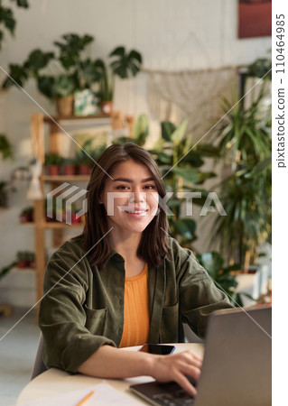 Young plant store worker posing at her workplace while working on laptop Young plant store worker posing at her workplace while working on laptop 110464985