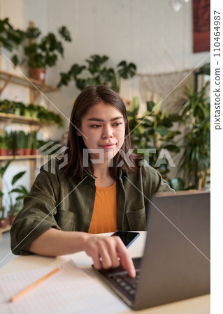 Young plant shop owner communicating online via her laptop while sitting at her workplace Young plant shop owner communicating online via her laptop while sitting at her workplace 110464987