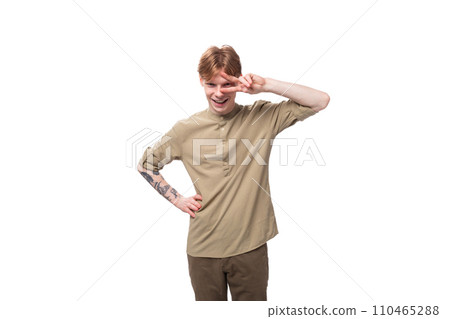young cheerful caucasian man with red hair is dressed in a khaki shirt and brown trousers young cheerful caucasian man with red hair is dressed in a khaki shirt and brown trousers 110465288