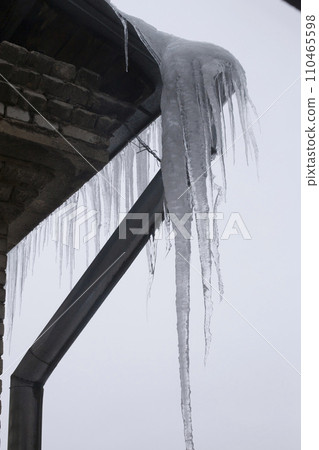 View from the window of huge ice icicles hanging on the roof and drainpipe. Dangerous ice icicles hang on the edge of the roof. View from the window of huge ice icicles hanging on the roof and drainpipe. Dangerous ice icicles hang on the edge of the roof. 110465598