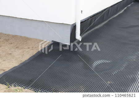 Laying a black waterproofing membrane around the foundation of a house. Construction of the blind area of the house. Reliable protection of the foundation from moisture. White pipe for draining 110465621